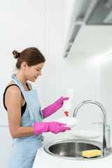 Young adult woman washing plates on kitchen