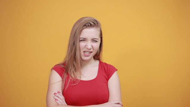 young blonde girl in red t-shirt over isolated orange background shows emotions