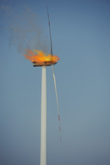 Eco power windturbine at sunny day under fire. Fire flames and black smoke escaping outside.