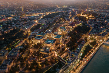 Budapest, Hungary - Aerial drone view of the illuminated Buda Castle Royal Palace at blue hour with Matthias Church at background, using a blurry tilt-shift effect