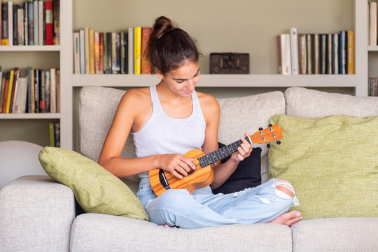 young girl playing ukulele sitting in a sofa at home