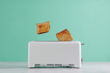 Roasted toast bread popping up of toaster with green wall, front view