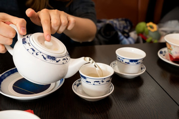 Fototapeta na wymiar Teapot in the hands of a girl pouring green tea into beautiful chinese cups