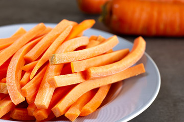 carrot sticks in blue rim dish with carrots in the background on gray surface