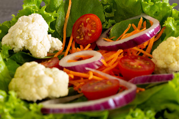 close up of green leaf salad with carrot, tomato, onion, cauliflower