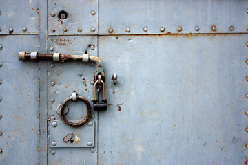 View of a closed iron door with rivets, bolts and a lock. Handle ring on a closed door.