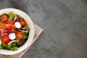 green leaf salad with carrot, tomato, onion and cheese on gray table top view