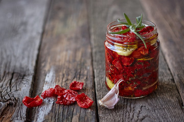 Close-up the jar of homemade sun-dried tomatoes with Provencal herbs, garlic and olive oil on a rustic wooden surface, selective focus