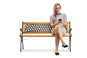 Young blond woman sitting on a bench and typing on a smartphone