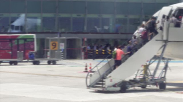 Defocused view of aircraft on airport runway tarmac with boarding passengers. Day view of unidentified travelers on an airport ladder connected to passenger jet at Naples International Airport. 