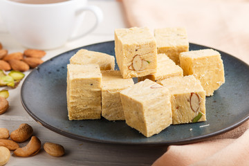 traditional indian candy soan papdi in a blue ceramic plate with almond, pistache and a cup of coffee on a white wooden background with orange textile. side view