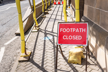 Red Sign on a pavement at the beginning of a construction area reading footpath closed