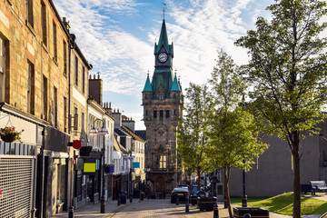 Obraz premium Pedestrian street lined with shops and traditional architecture in a town centre at sunset. Dunfermline, Scotland, UK.