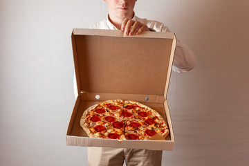 Young man is opening a delivery cardboard box with hot pepperoni pizza with champignon mushrooms - obrazy, fototapety, plakaty