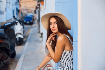 Portrait of young elegant woman in straw hat sitting on the street.