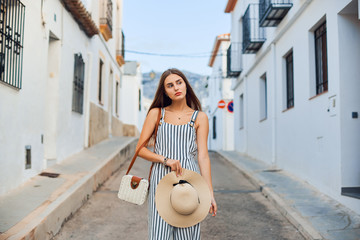 Young elegant woman with straw hat walking on the narrow streets of the old town.