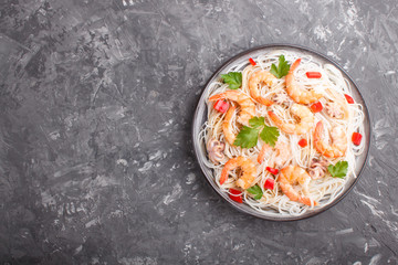 Rice noodles with shrimps or prawns and small octopuses on gray ceramic plate on a black concrete background. Top view.