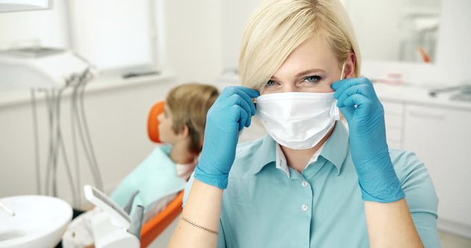 Attractive female dentist taking protective mask off and smiling to camera, service quality