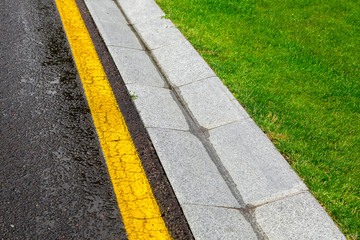 rainwater in the canal is a cement ditch of a drainage system on the side of wet tarmac road with yellow line and a green lawn on roadside environment.