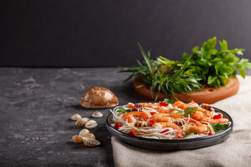 Rice noodles with shrimps or prawns and small octopuses on gray ceramic plate on a black concrete background. side view, copy space.