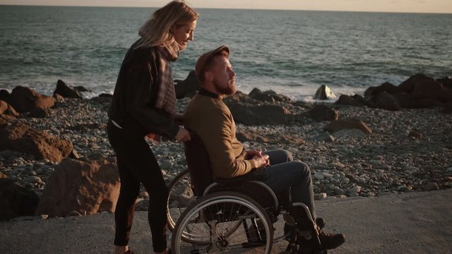Woman taking care of disabled husband and walking with him by the sea