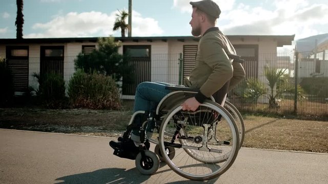 Young man with paralyzed legs in wheelchair is walking alone in city streets