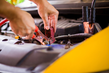 selective focus charging yellow car with electricity trough cables. first connect anode then follow connect negative connector battery