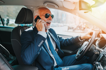 Senior good looking businessman talking on mobile phone while driving his car .