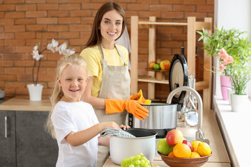 Woman and her little daughter washing multi cooker in kitchen
