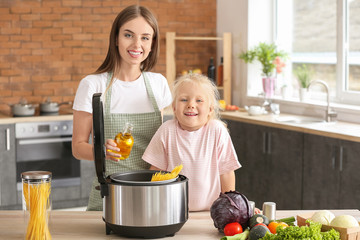 Woman and her little daughter using modern multi cooker in kitchen