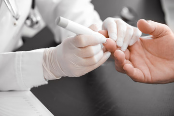 Doctor taking blood sample of diabetic man in clinic, closeup