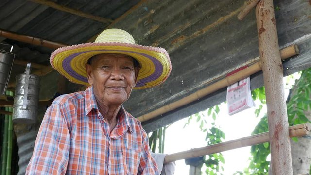An elderly male farmer in the Asian countryside sitting in a small cottage with zinc roof after working hard on the farm.