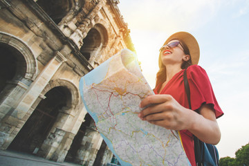 Happy smiling tourist girl in bright red dress holding a map in hands while standing in front of Nimes arena