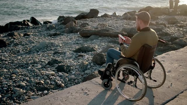 Disabled man surfing net on mobile while relaxing by the sea