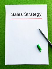Paper with text sales strategy on green table.