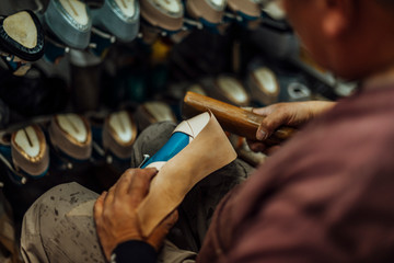 Fototapeta na wymiar Hands of an old and experienced worker in the handmade footwear industry, performing gluing tasks, placing genuine sole at the base of a luxury handmade shoe.