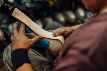 Hands of an old and experienced worker in the handmade footwear industry, performing gluing tasks, placing genuine sole at the base of a luxury handmade shoe.
