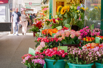 Fototapeta na wymiar View of colourful various flowers in plastic box are sold at corridor in front of flower stall or floral shop is located in outdoor market in Europe. Typical atmosphere of flower store. 
