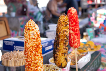 Several varieties of Mexican elote snacks on display at a food stand.