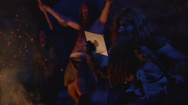 Happy ancient illiterate caveman using modern computer tablet talking on video call socializing. Homo sapiens. Life in primal tribe.