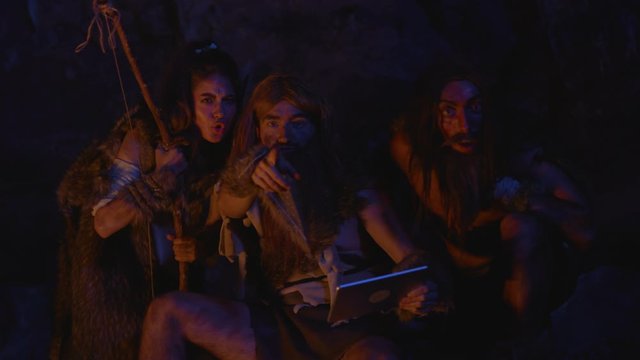 Prehistoric tribe family using future tablet computer at night. Wild people aborigines noticing somebody looking with anger and fear.