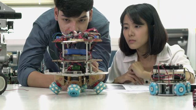 Asian couple engineer students are assembling and testing electric robotics arm in modern laboratory. Concept of configuration, technological developments and innovation.
