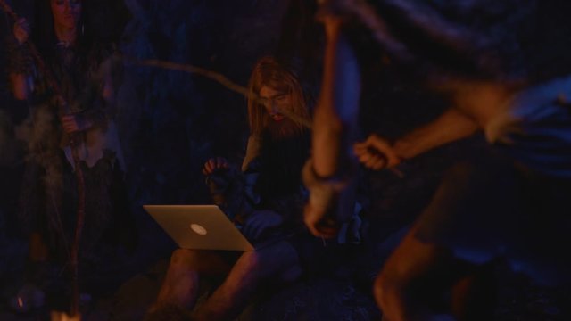 Primitive homo sapiens family at bonfire. Curious barbarian nomadic neanderthal using modern computer laptop learning technology. Evolution concept.