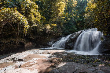 Natural blurred background of waterfalls, fast-flowing currents and water droplets from the wind blowing among the rocks and surrounded by big trees, spontaneous beauty