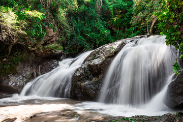 Natural blurred background of waterfalls, fast-flowing currents and water droplets from the wind blowing among the rocks and surrounded by big trees, spontaneous beauty