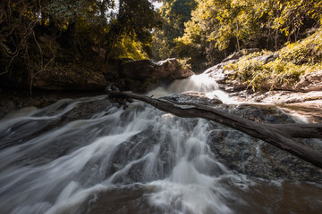 Natural blurred background of waterfalls, fast-flowing currents and water droplets from the wind blowing among the rocks and surrounded by big trees, spontaneous beauty