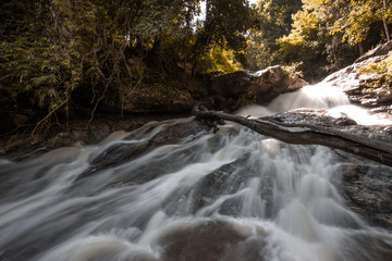 Natural blurred background of waterfalls, fast-flowing currents and water droplets from the wind blowing among the rocks and surrounded by big trees, spontaneous beauty