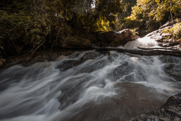 Natural blurred background of waterfalls, fast-flowing currents and water droplets from the wind blowing among the rocks and surrounded by big trees, spontaneous beauty