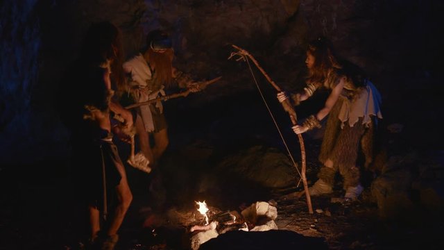 Ancient primitive family of neanderthals using modern VR glasses having fun on ritual party at bonfire. Prehistory and future technology. Homo sapiens.