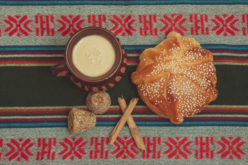 Pan de muerto y taza de chocolate sobre una mesa con mantel típico mexicano. Con ingredientes de...